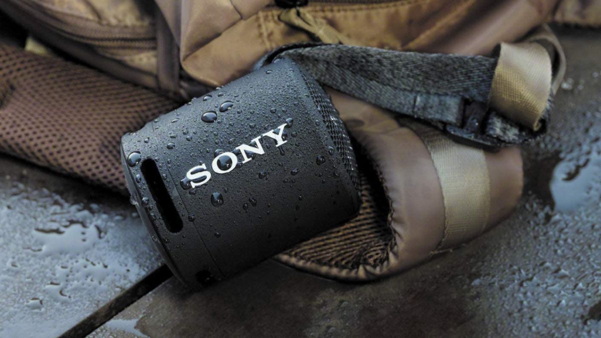 Alto-falante Bluetooth sem fio Sony SRS-XB13 encharcado de água, deitado ao lado de uma mochila