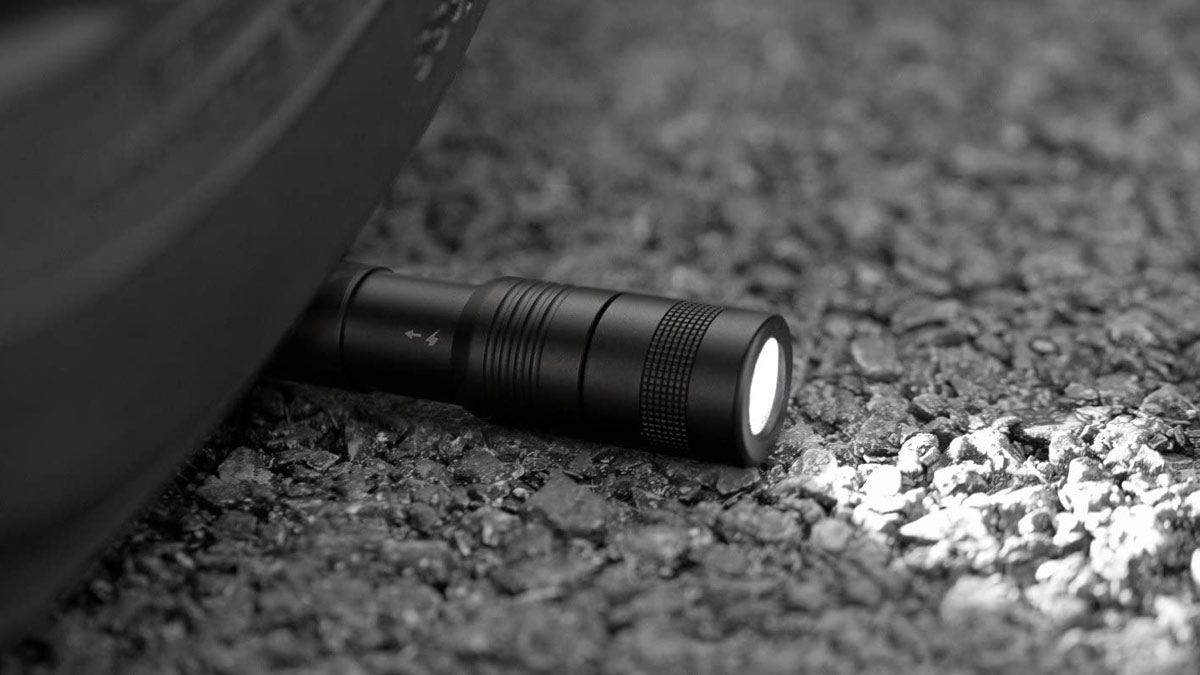 Uma lanterna robusta com caneta Anker pousada na estrada sob um pneu.