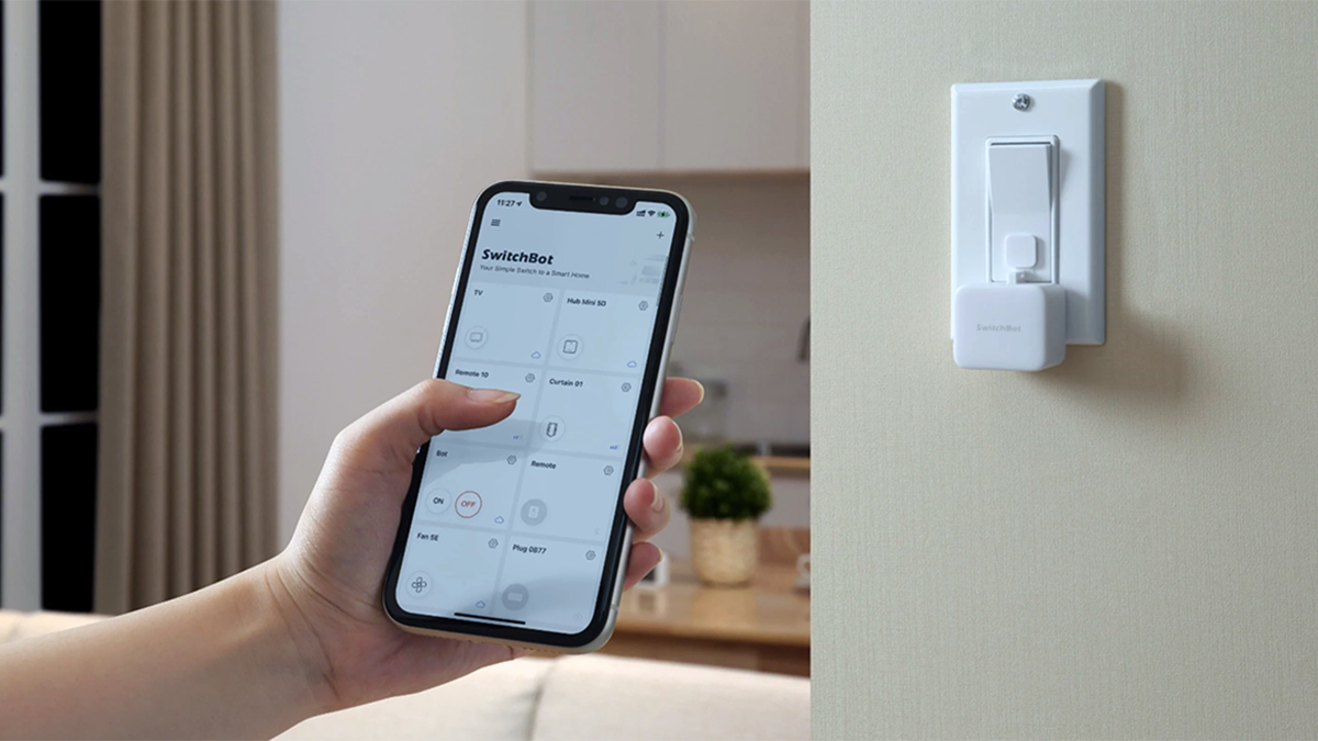 Mão segurando o smartphone com o aplicativo SwitchBot em primeiro plano e o SwitchBot Bot em segundo plano