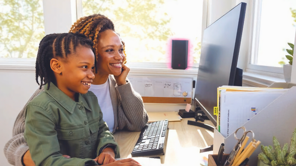 Uma mulher e sua filha usando um computador desktop com um gateway Wi-Fi 5G da T-Mobile em segundo plano