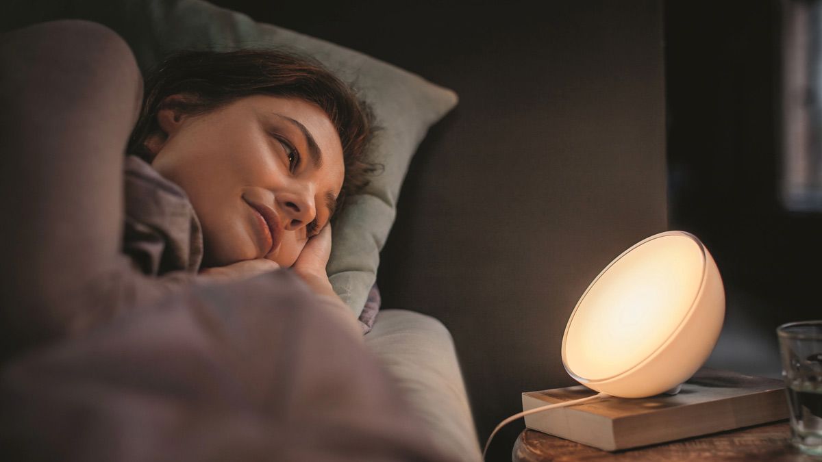 Uma mulher se prepara para dormir, olhando para uma luz inteligente Hue Go brilhante em sua mesa de cabeceira.