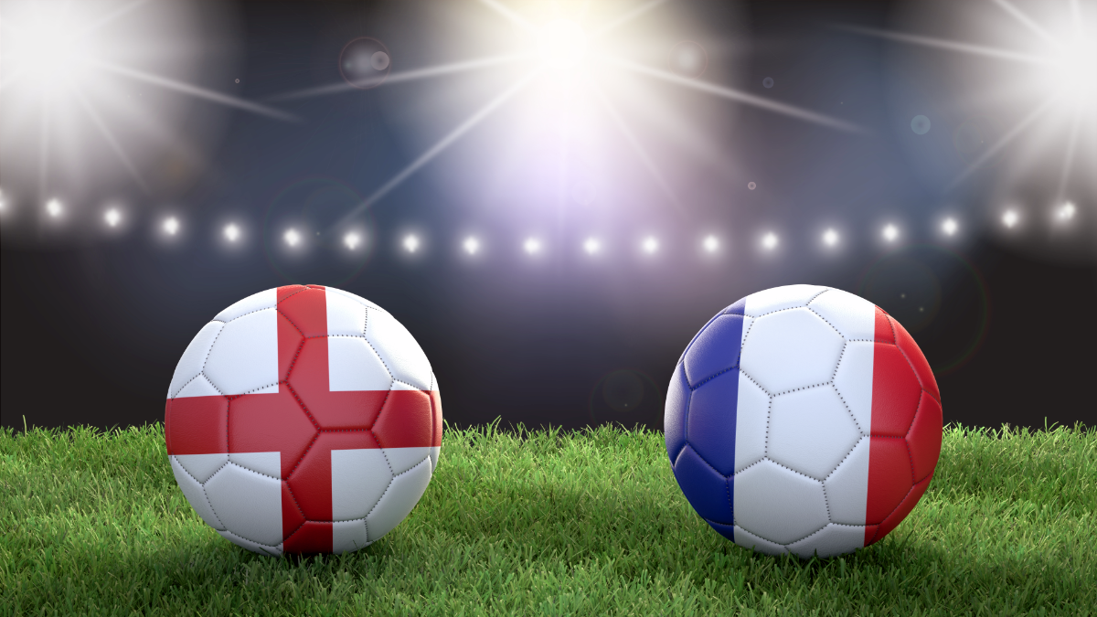 Duas bolas de futebol estampadas com as cores das bandeiras inglesa e francesa estão em um campo de futebol sob a luz do estádio