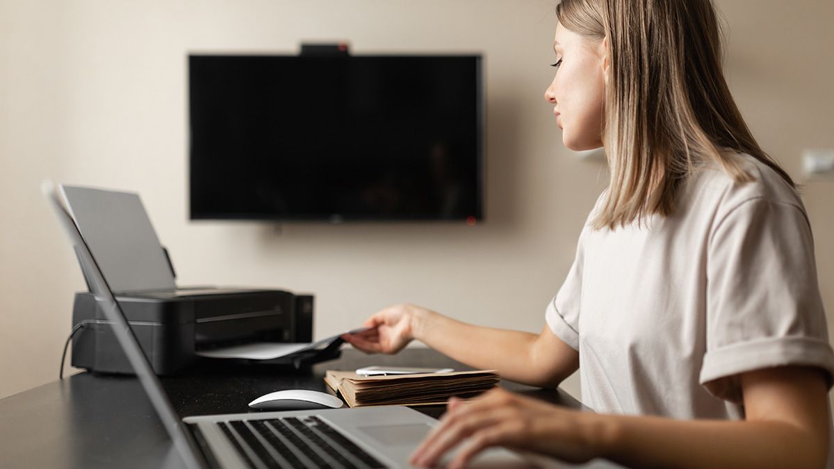 Alguém usando laptop e impressora em uma sala com uma televisão grande.