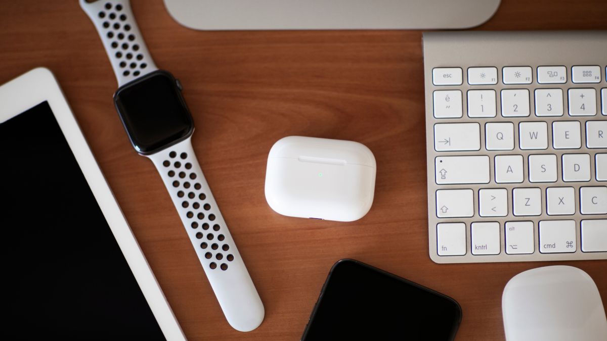 Um case AirPods Pro em uma mesa de madeira cercada por outros dispositivos Apple.