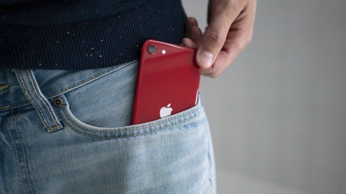 Um iPhone SE vermelho (versão 2022) sendo retirado do bolso da calça jeans de uma pessoa.