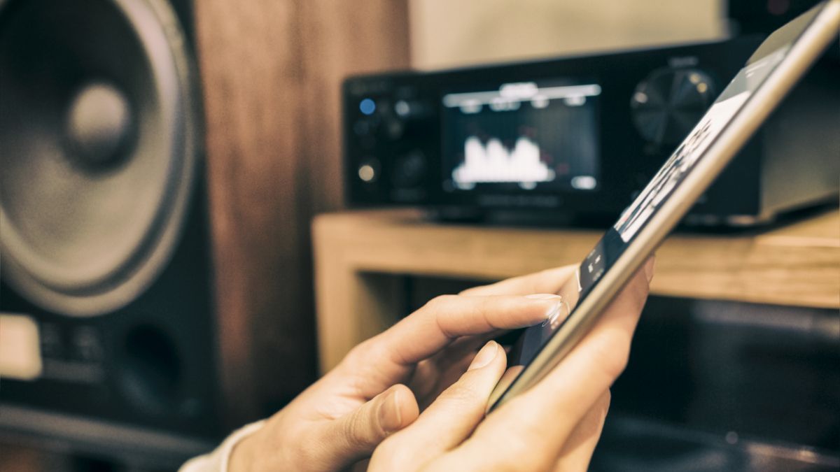 Closeup de mãos controlando um sistema de áudio doméstico com um tablet.