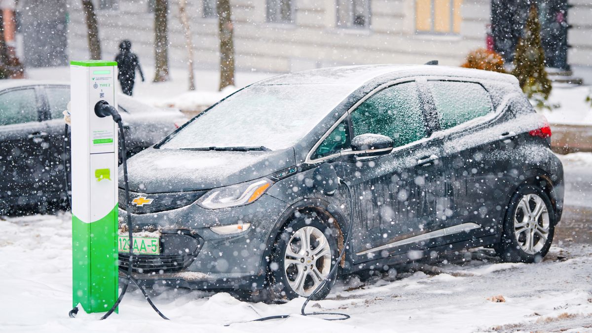 Um carro elétrico Chevy Bolt conectado a uma estação de carregamento enquanto a neve cai.