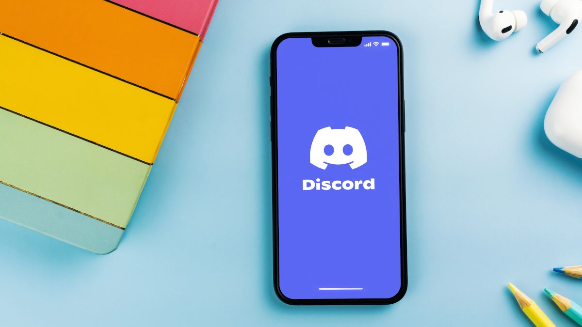 Smartphone mostrando o logotipo do Discord ao lado dos AirPods, lápis e controlador de jogo.