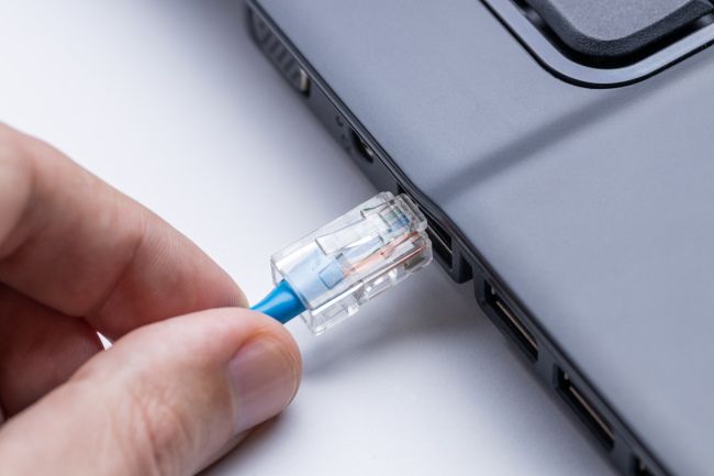Pessoa conectando um cabo Ethernet a um laptop.