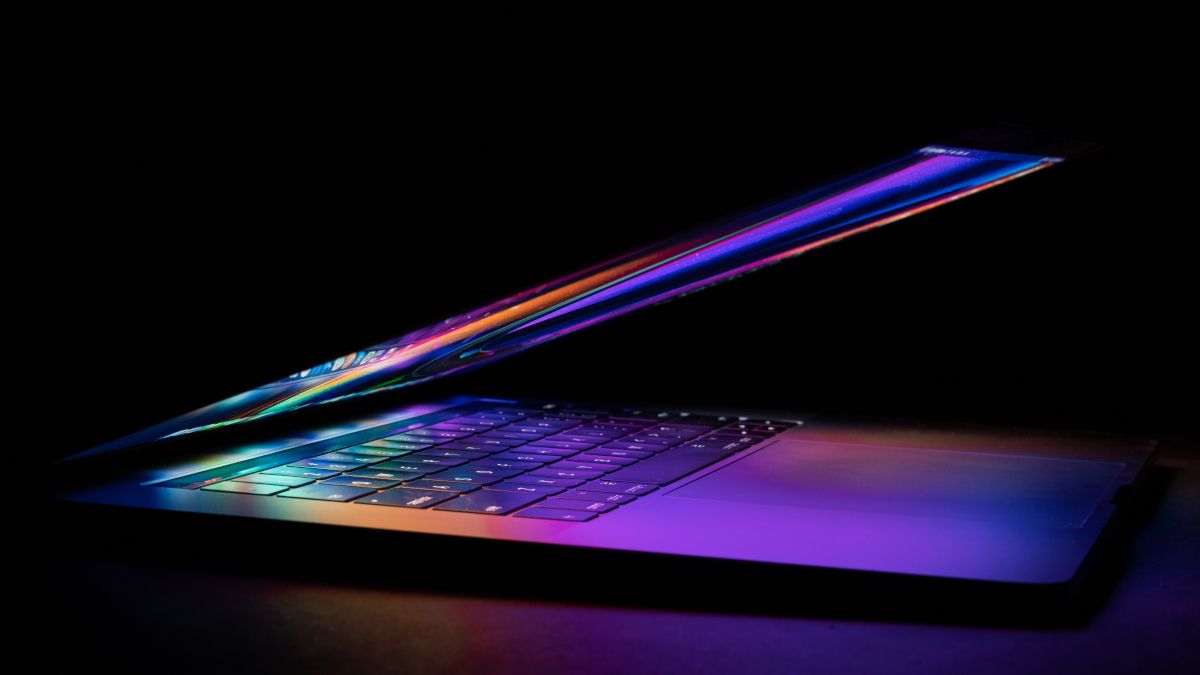 Um MacBook semifechado com cores brilhantes da tela refletidas no teclado.