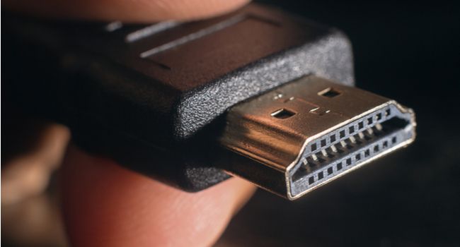 Close de um conector HDMI entre os dedos de uma pessoa.