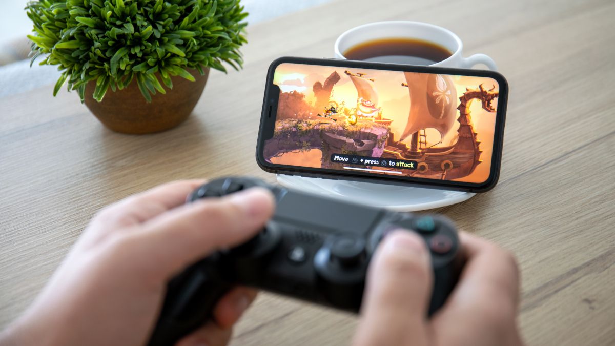 Pessoa segurando um controle DualShock 4 em frente a um iPhone 11 jogando Rayman Adventures.