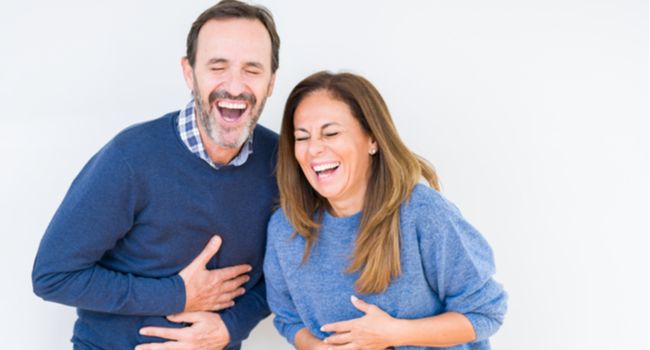 Um casal apertando a barriga de tanto rir.