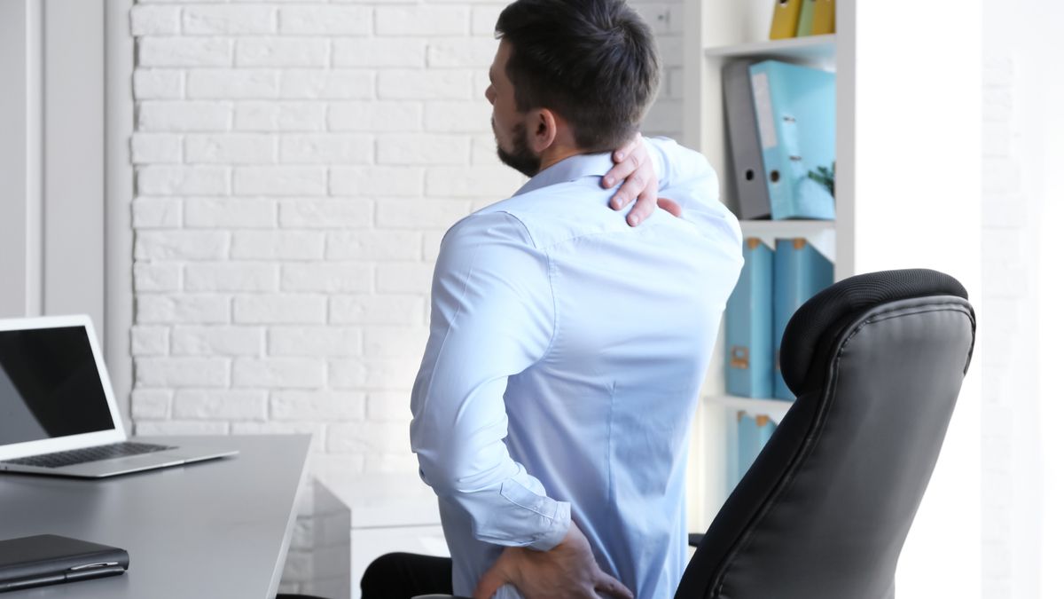 Homem sentado em uma cadeira de escritório e segurando as costas com dor.