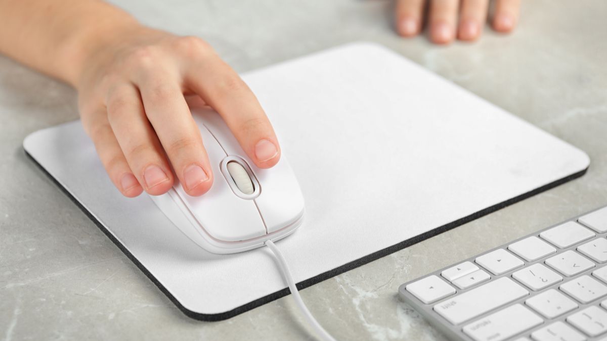 Close da mão de uma mulher usando um mouse com fio em um mouse pad branco.