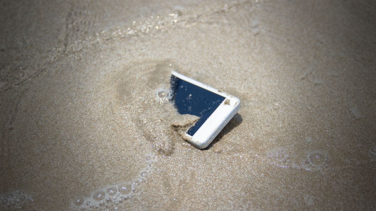 Um smartphone na areia do oceano com água salgada.