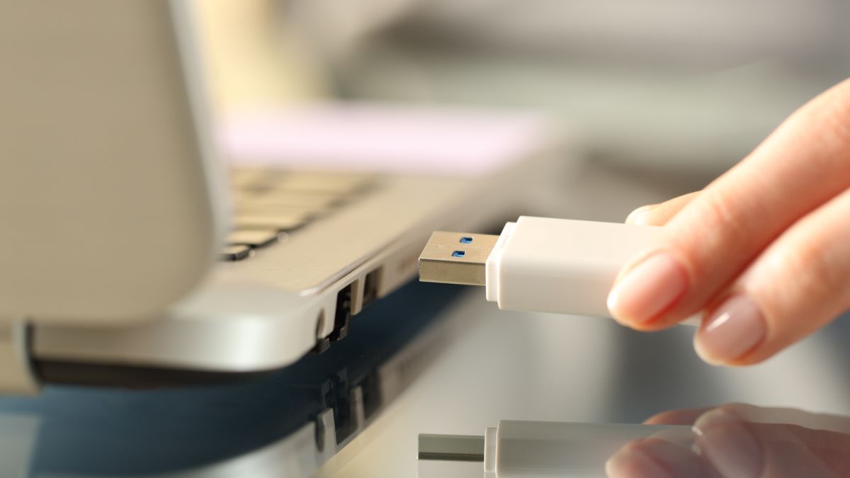 Close da mão de uma mulher conectando uma unidade USB em um laptop.