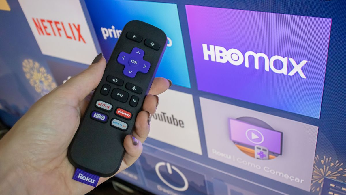 Controle remoto Roku em mãos na frente da tela inicial do Roku.