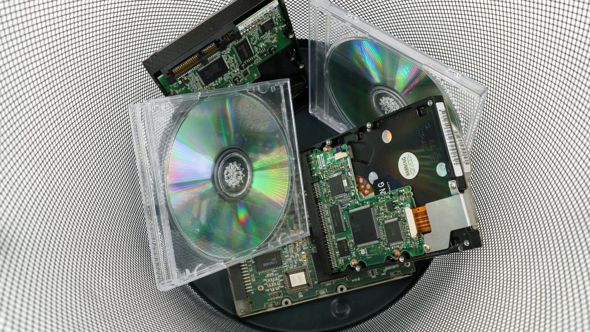 Discos compactos antigos e hardware de computador descartados em uma lixeira.