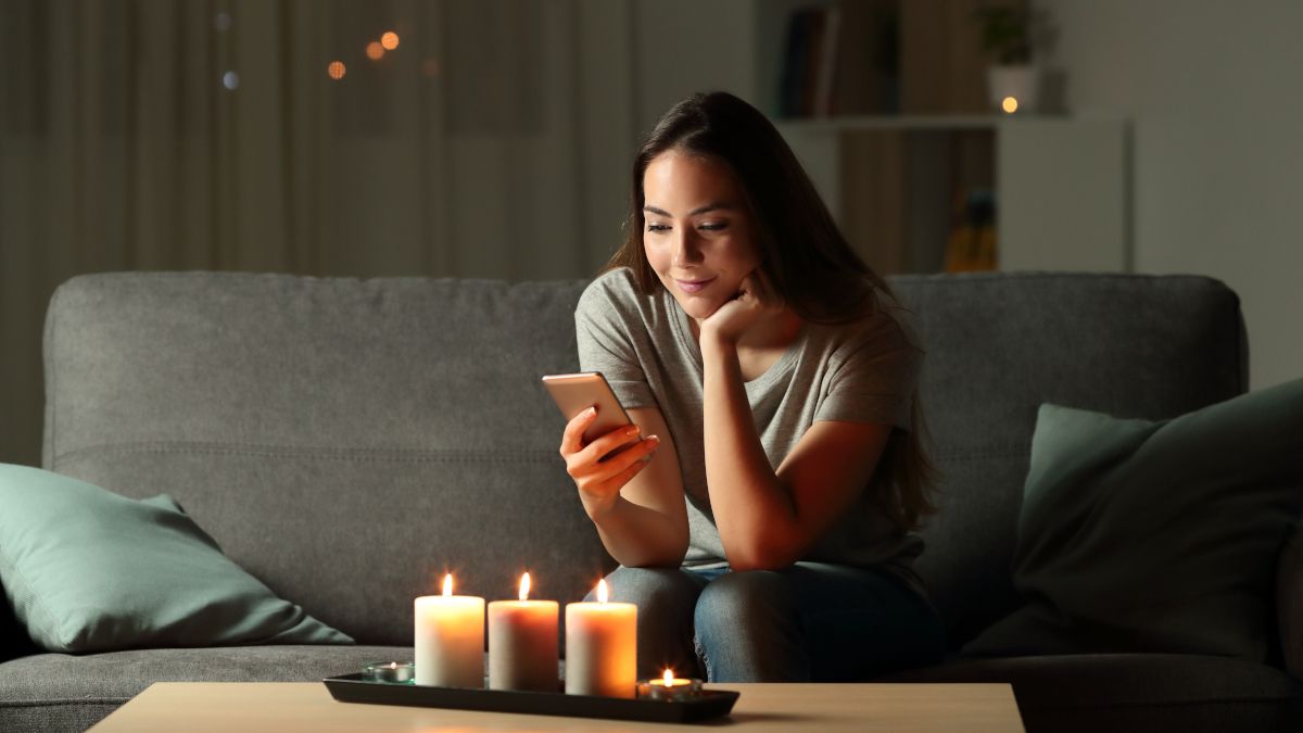 Mulher usando um smartphone em uma sala decorada com velas acesas.
