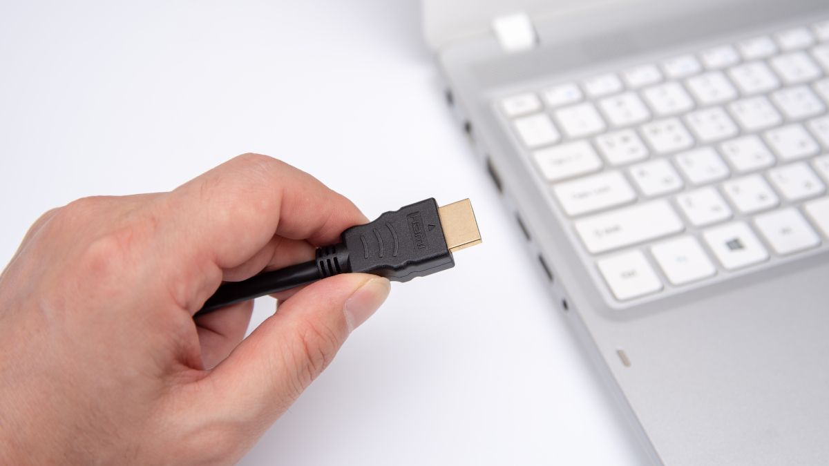 Pessoa conectando um cabo HDMI a um laptop.