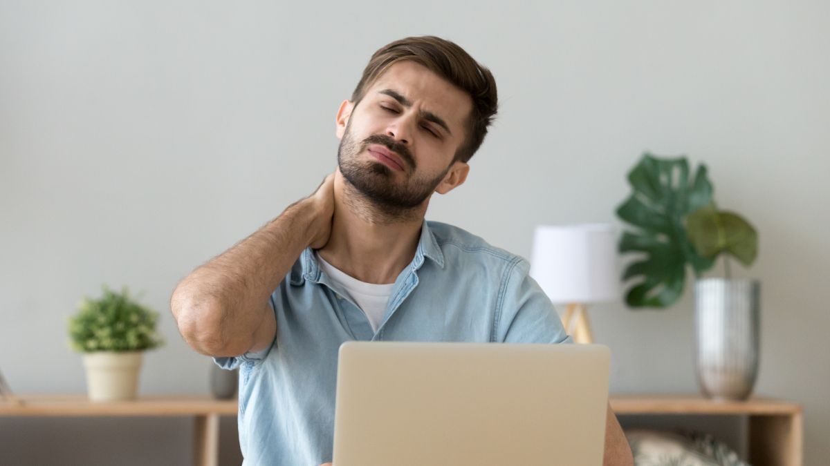 Homem sentado em frente a um laptop e esfregando o pescoço de dor.