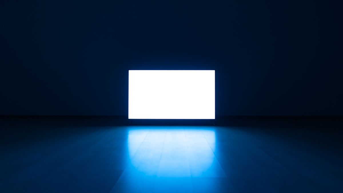 Televisão no chão de uma sala escura com luz azul refletida no chão.