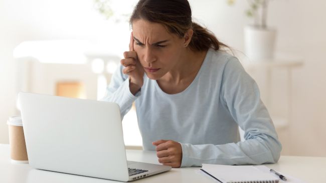 Mulher esticando o pescoço para ver a tela de um laptop.