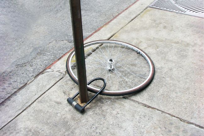 Uma única roda de bicicleta presa a um poste com uma trava, o resto da bicicleta provavelmente roubado.