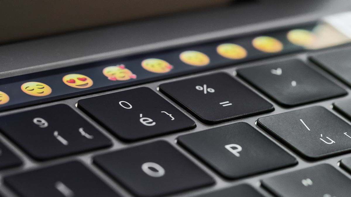 Close de um teclado do MacBook Pro com a Touch Bar apresentando emoji em foco.