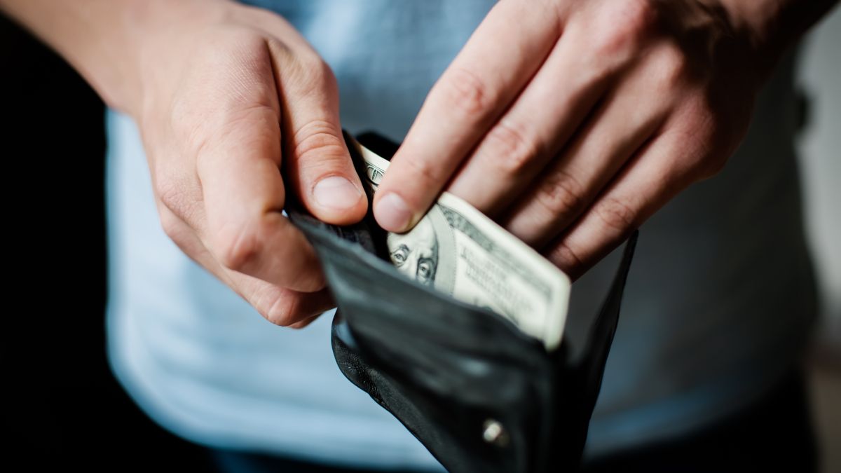 Mãos de uma pessoa tirando uma nota de US$ 100 de uma carteira.
