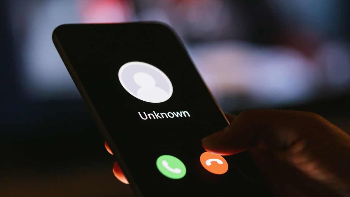 A mão de uma pessoa segurando um smartphone no escuro, com uma chamada de um chamador desconhecido em exibição.