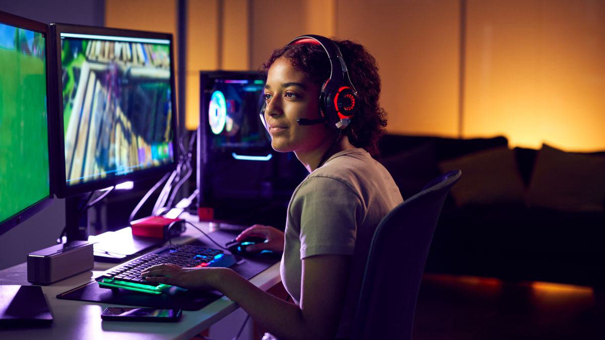 Mulher jogando videogame na configuração do computador com monitor duplo.