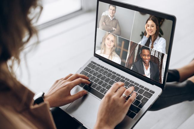 Mulher usando um laptop com uma grade de pessoas em uma videoconferência na tela.