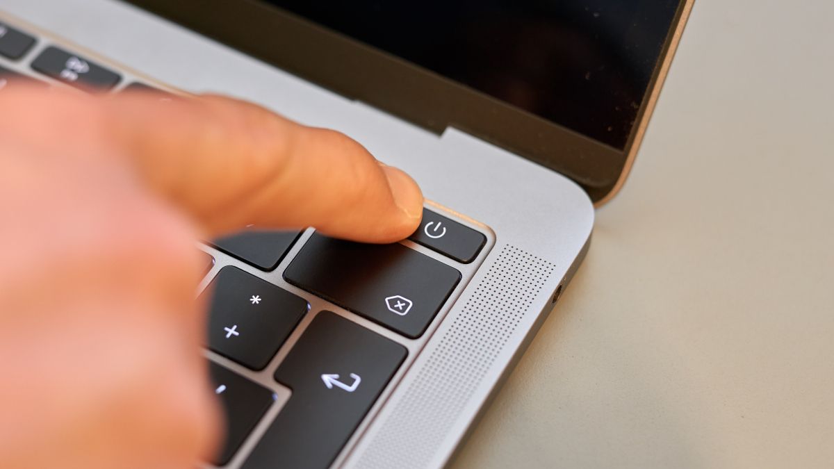O dedo de uma pessoa pressionando o botão liga/desliga em um notebook.