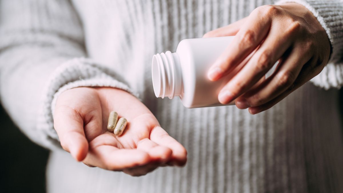 Mãos de uma pessoa segurando pílulas de ervas medicinais e uma garrafa de plástico branca.