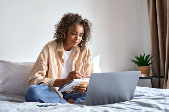 Mulher sentada em uma cama com um laptop na frente dela.