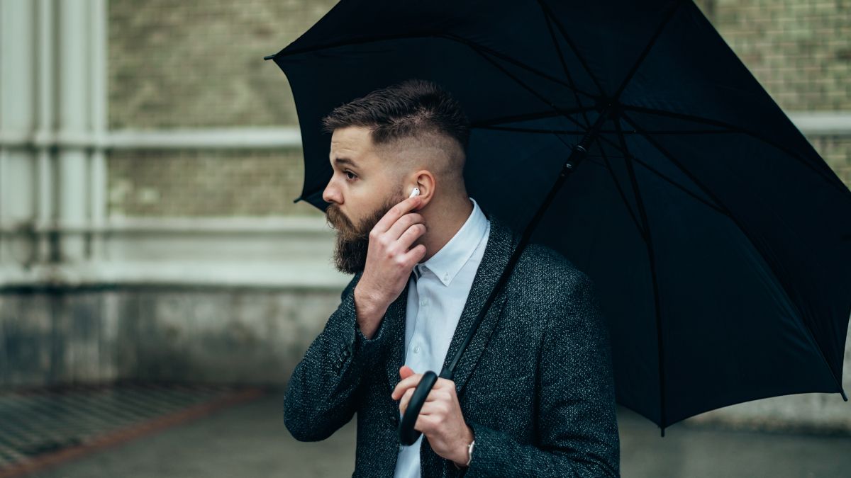 Homem colocando AirPods no ouvido enquanto segura um guarda-chuva na chuva.