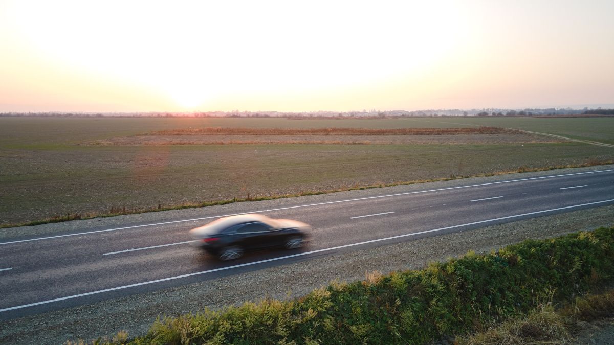 Vista aérea de um veículo elétrico acelerando em um cruzamento de rodovia em um campo aberto ao pôr do sol.