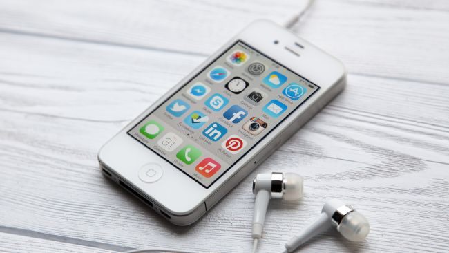Um iPhone 4 com fones de ouvido em uma mesa de madeira branca.
