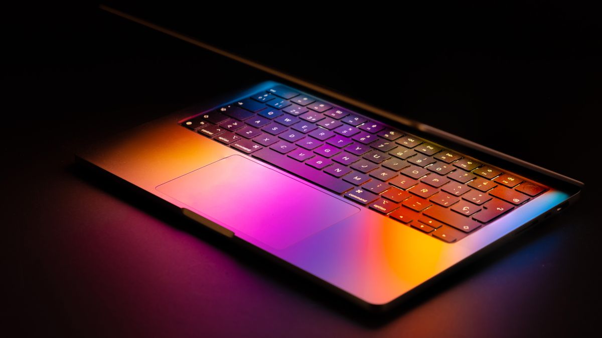 Um Apple MacBook com o laptop parcialmente levantado e a luz da tela refletida no teclado.