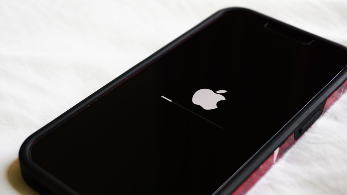 Close de um iPhone em uma mesa branca com o logotipo da Apple e a barra de progresso da atualização de software visíveis na tela.