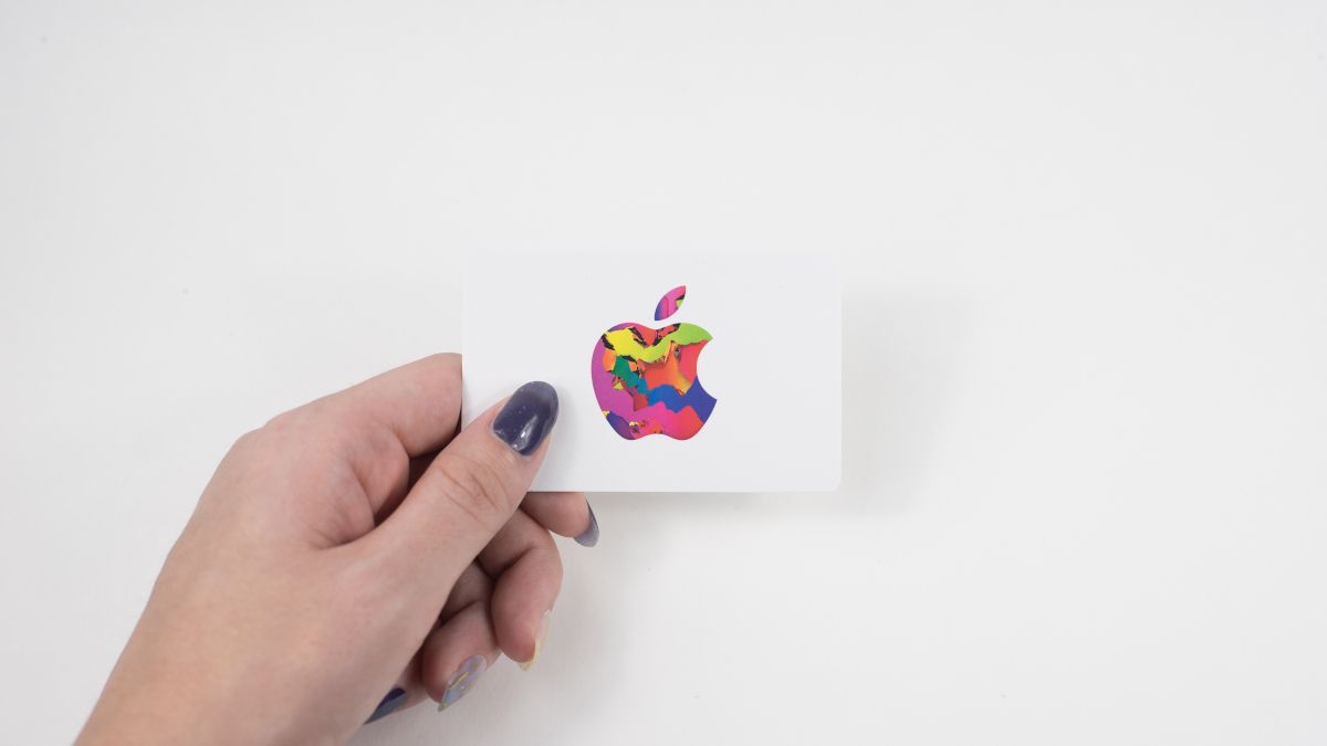 A mão de uma pessoa segurando um vale-presente da Apple contra um fundo branco.