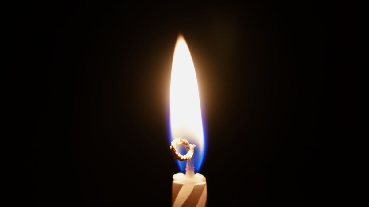 Uma única chama em uma vela de aniversário listrada contra um fundo escuro.