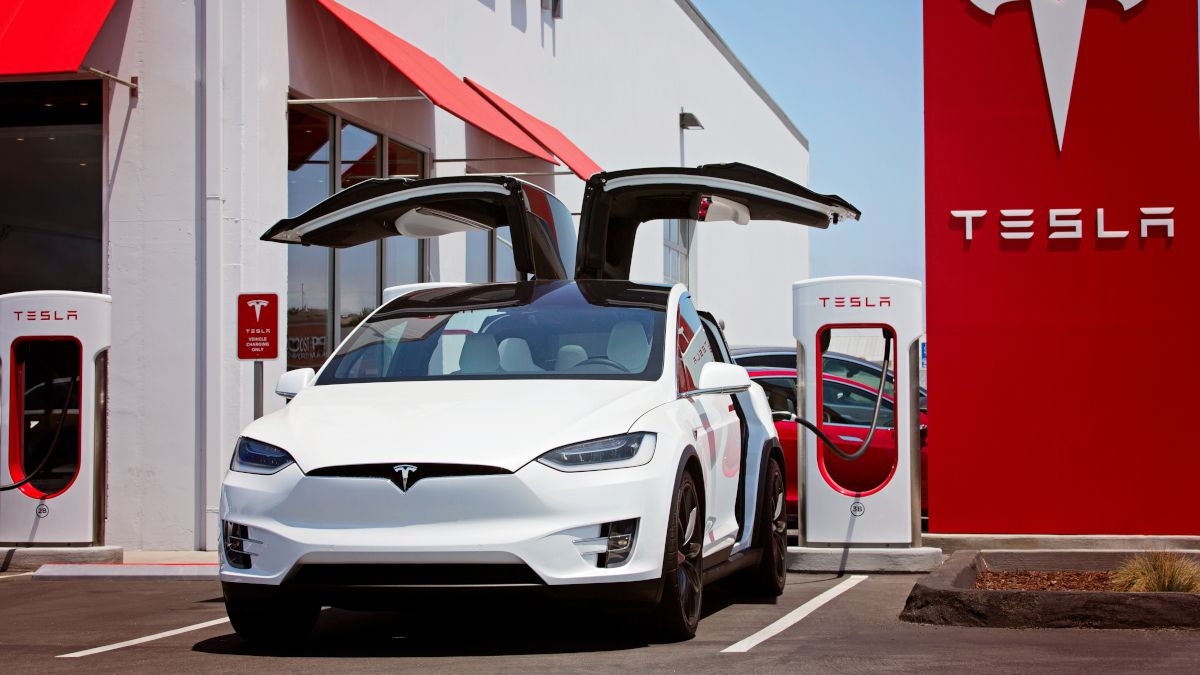 Carro Tesla conectado a uma estação de carregamento e com as portas em forma de asa de falcão abertas.