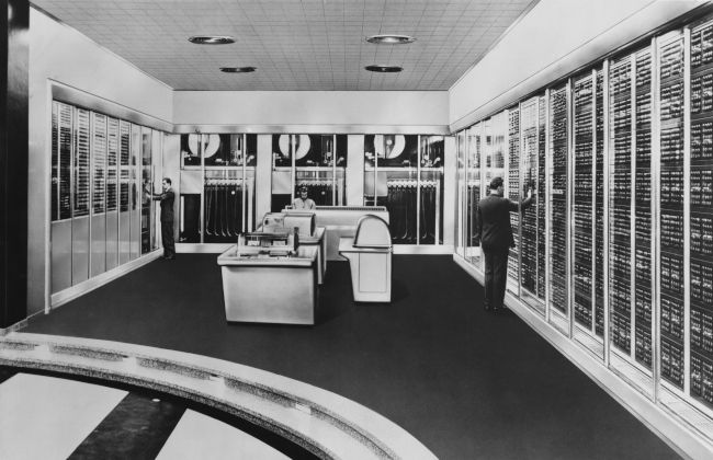 Foto em preto e branco de pessoas trabalhando em um computador mainframe de meados do século.