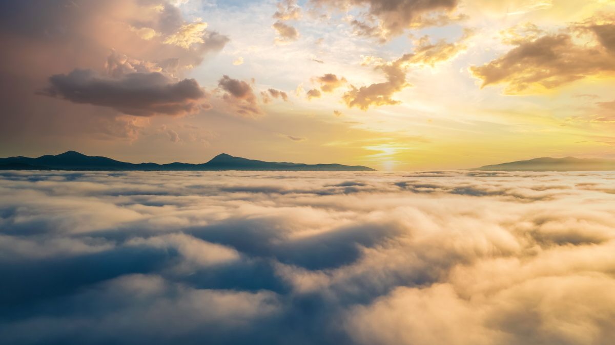 Uma vista aérea de um pôr do sol sobre nuvens densas com montanhas no horizonte.