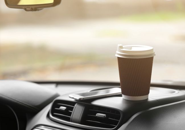 Um smartphone e uma xícara de café de papel em cima do painel de um carro.