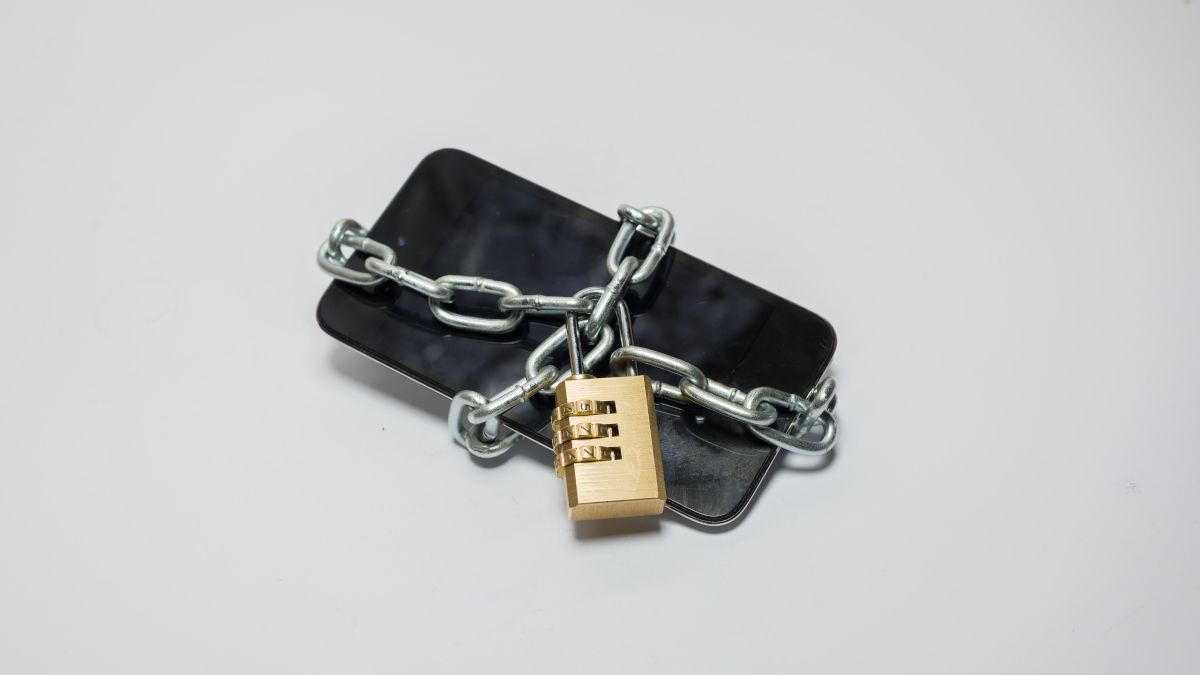 Smartphone enrolado em uma corrente de metal com um cadeado que o protege.