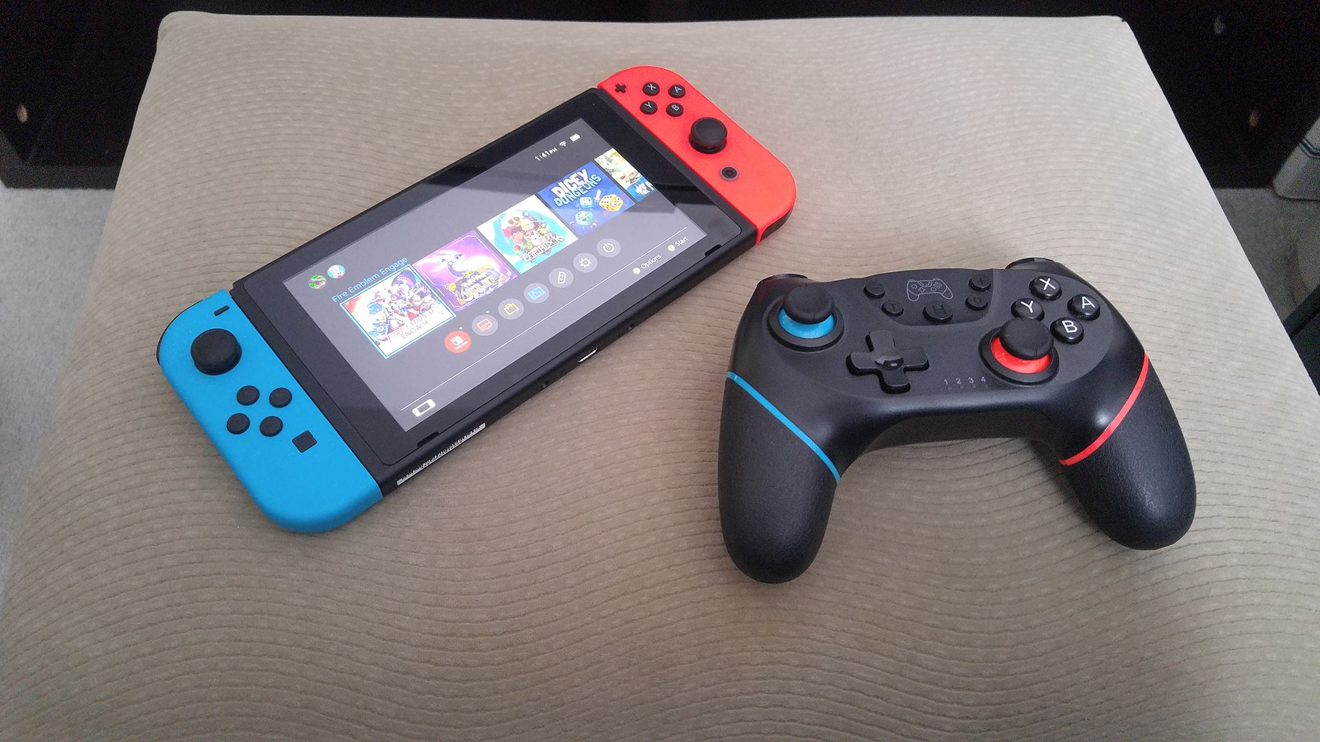 Um tablet Nintendo Switch com controles Joy-Con acoplados ao lado de um controle Switch Pro em um apoio para os pés bege.